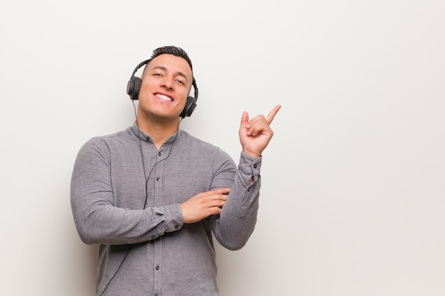 Junger lateinischer Mann, der Musik zeigt auf die Seite mit dem Finger hört