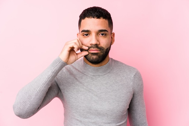 Junger lateinischer Mann gegen eine rosa Wand lokalisiert mit den Fingern auf den Lippen, die ein Geheimnis halten.