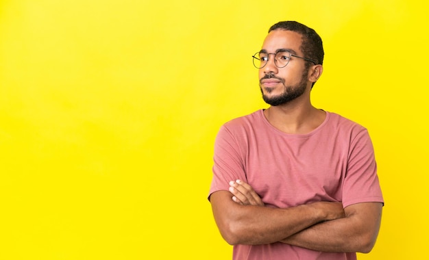 Junger lateinischer Mann isoliert auf gelbem Hintergrund, der zur Seite schaut