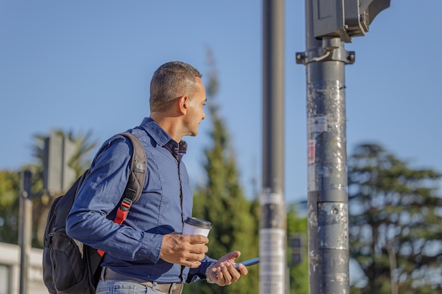 Junger Latino-Mann mit einer Einwegtasse Kaffee in der Hand beobachtet den Verkehr