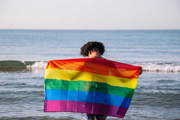 Junger Latino-Mann mit LGTbi-Flagge am Strand