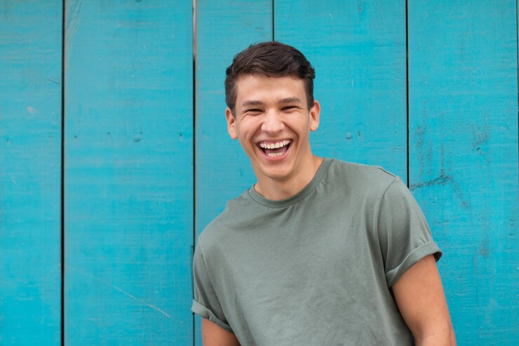 Junger Latino mit authentischem Lachen, im Hintergrund eine für Latino-Häuser typische blaue Tür.