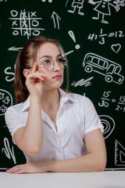 Junger Lehrer sitzt nahe Tafel im Klassenzimmer