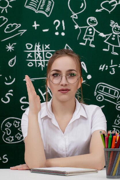 Junger Lehrer sitzt nahe Tafel im Klassenzimmer