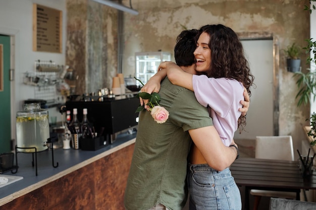 Junger liebevoller Mann, der seine fröhliche Freundin mit rosa Rose umarmt