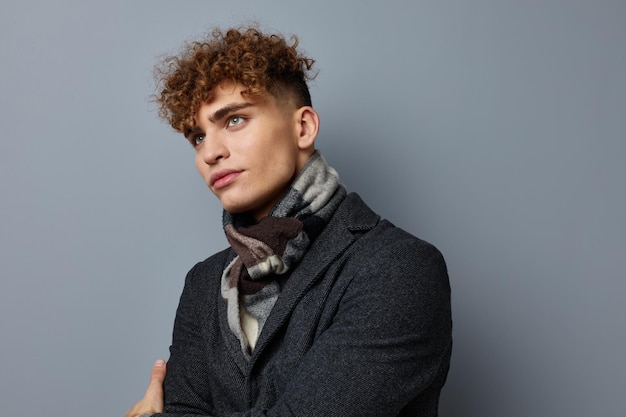 Junger lockiger Mann in einem Mantel im Studio posiert auf grauem Hintergrund