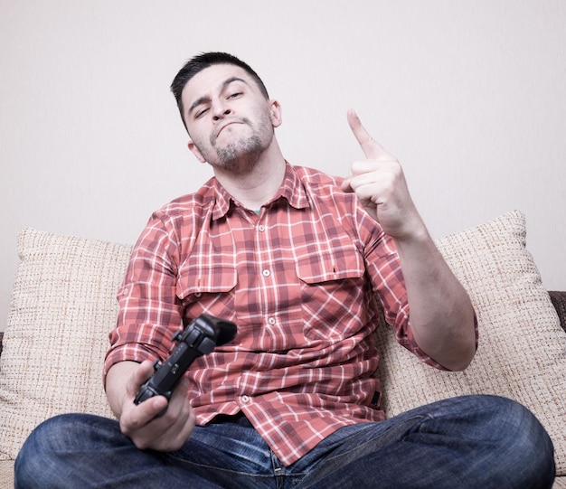 Junger lustiger Mann, der Videospiele spielt, sitzt auf dem Sofa und hält die Fernbedienung in der Hand