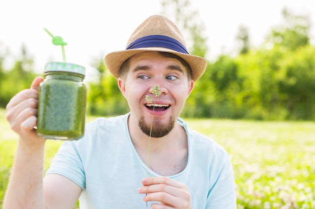 Junger lustiger Mann hält Detox-Smoothie mit Trinkhalm. Konzept des gesunden Lebensstils, der Leute und des Essens.