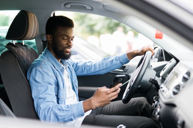 Junger männlicher Afroamerikaner, der sein Telefon hält, während er sein Auto fährt