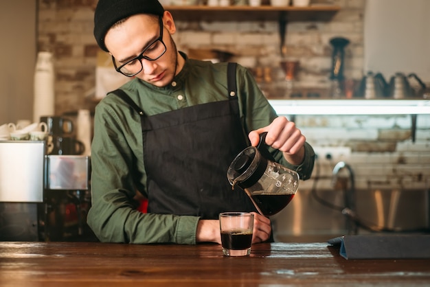 Junger männlicher Barmann gießt Kaffee in ein Glas. Kaffeehaus auf dem Hintergrund.