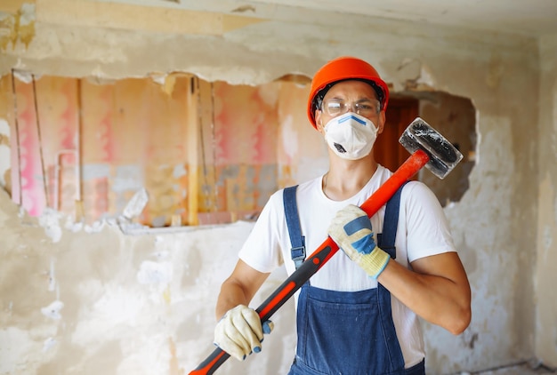 Junger männlicher Baumeister mit Schutzhelm, der Werkzeuge hält Wohnungsreparatur- und Renovierungskonzept