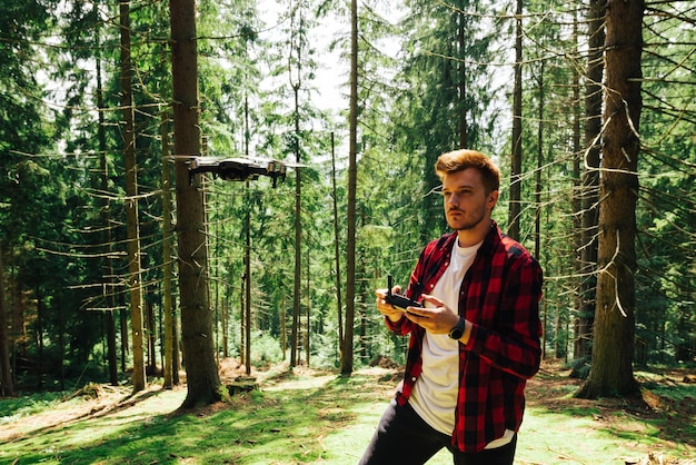 Junger männlicher Bediener steuert eine Drohne in einem Bergwald mit wunderschöner Natur