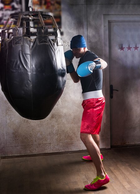 Junger männlicher Boxer im Boxhandschuhtraining mit Boxsack in einer Turnhalle