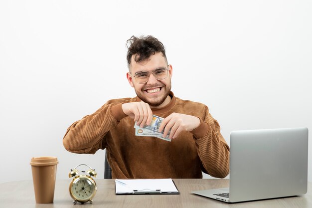 Junger männlicher Buchhalter, der an seinem Schreibtisch sitzt und Bargeld zeigt.