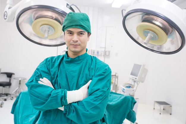 Junger männlicher Doktor, der zur Kamera mit attraktivem Lächeln Operationsraumhintergrund schaut