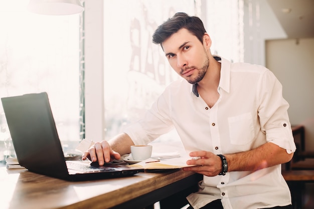 Junger männlicher Freiberufler, der Laptop beim Sitzen in der Kaffeestube verwendet