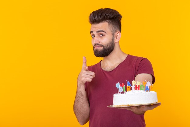 Junger männlicher Hipster mit einem Bart, der einen Kuchen mit der Inschrift alles Gute zum Geburtstag hält