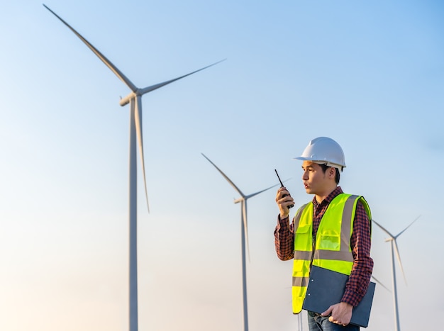 Junger männlicher Ingenieur, der Walkie-Talkie verwendet, um System gegen Windkraftanlagenpark zu überprüfen