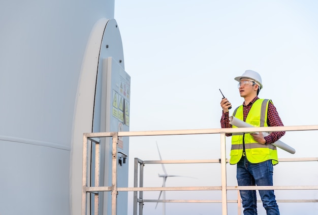 Junger männlicher Ingenieur, der Walkie-Talkie verwendet, um System gegen Windkraftanlagenpark zu überprüfen