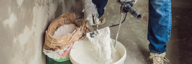 Junger männlicher Maler knetet Kitt mit Wasser in einem Eimer mit einem Handmixer für Baumischungen