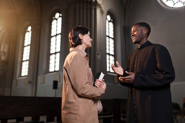 Junger männlicher Priester und Frau unterhalten sich in der Kirche, während sie eine Bibel halten