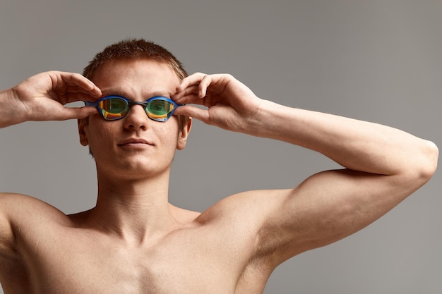 Junger männlicher Schwimmer, der sich auf den Start vorbereitet, Nahaufnahme eines Schwimmers in einer Maske und einem Hut, grauer Hintergrund, Kopierraum, Schwimmkonzept.