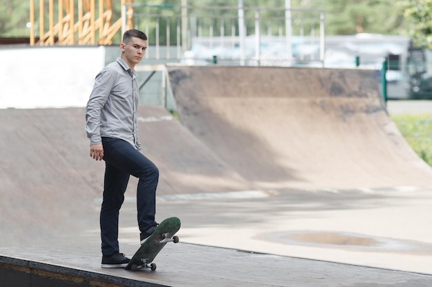 Junger männlicher Skateboarder, der sich darauf vorbereitet, Sketchboard zu fahren, indem er es an einem warmen Sommertag mit einem Fuß im Park anhebt