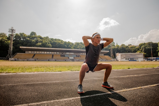 Junger männlicher Sprinter, der sich auf dem Stadion ausdehnt.