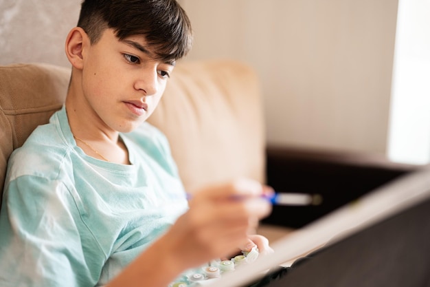 Junger männlicher Teenager malt Bild nach Zahlen auf Leinwand im heimischen Wohnzimmer Hobby und Freizeit ca