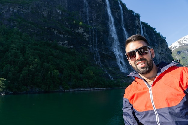 Junger männlicher Tourist am Sieben-Schwestern-Wasserfall im Geiranger-Fjord in Norwegen glücklich