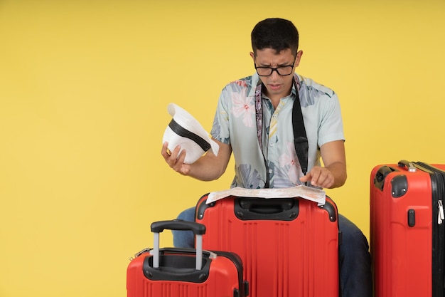 Junger männlicher Tourist, der sich besorgt fühlt, verloren mit seinen roten Koffern, die mit einer Karte suchen, wohin sie gehen sollen