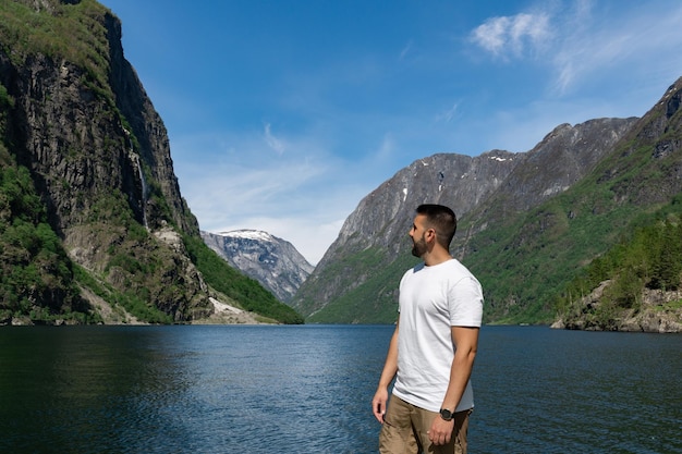 Junger männlicher Tourist im Vordergrund und hinter ihm die hohen Berge und der Fjord in Gudvangen Norwegen