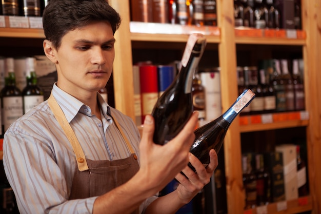 Junger männlicher Winzer, der an seinem Geschäft arbeitet und zwei Weinflaschen hält, kopiert Platz