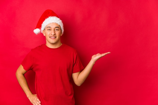 Junger Mann am Weihnachtstag einen Kopienraum auf einer Palme zeigend und eine andere Hand auf Taille halten.