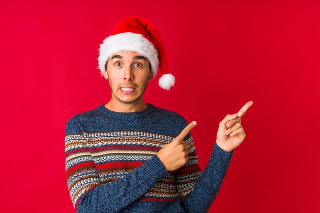 Junger Mann am Weihnachtstag lächelnd, mit dem Zeigefinger weg freundlich zeigend.