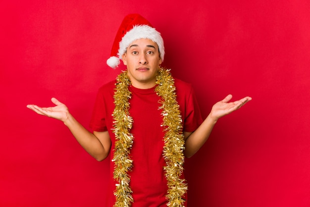 Junger Mann am Weihnachtstag Schultern in fragender Geste zweifelnd und zuckend.