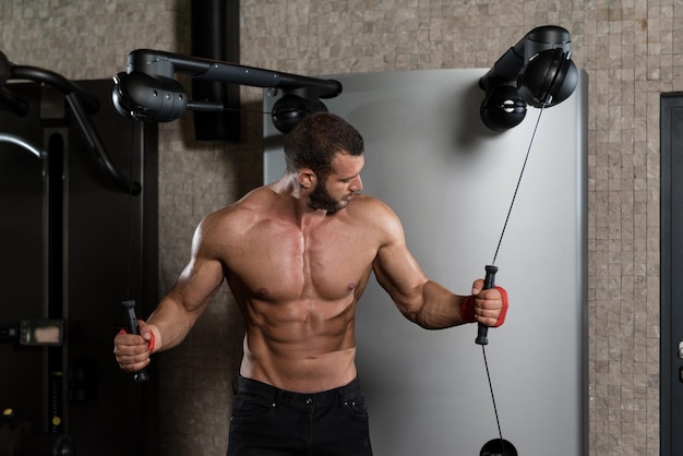 Junger Mann arbeitet an seiner Brust mit Kabelübergang in einem modernen Fitness-Studio