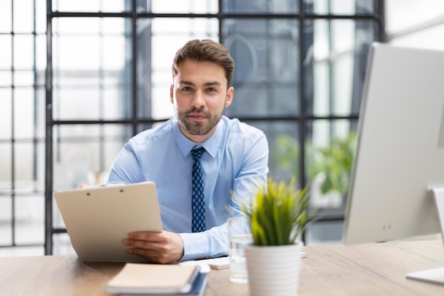 Junger Mann arbeitet mit Papieren, während er im Büro sitzt Erfolgreicher Unternehmer studiert Dokumente mit aufmerksamem und konzentriertem Blick