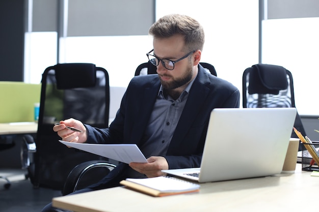 Junger Mann arbeitet mit Papieren, während er im Büro sitzt.