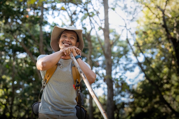 Junger Mann asiatischer Trekking zwischen Bäumen mit Rucksack Junger Mann genießt allein im Wald Camping Wandern Reisen Suche nach Abenteuer Konzept.