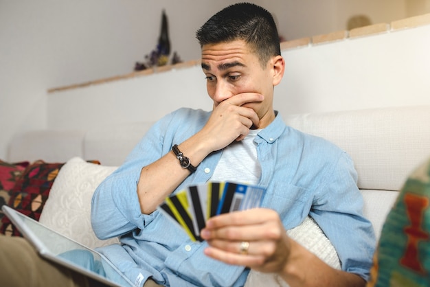 Junger Mann auf dem Sofa zu Hause mit Tablette beim Online-Einkauf.