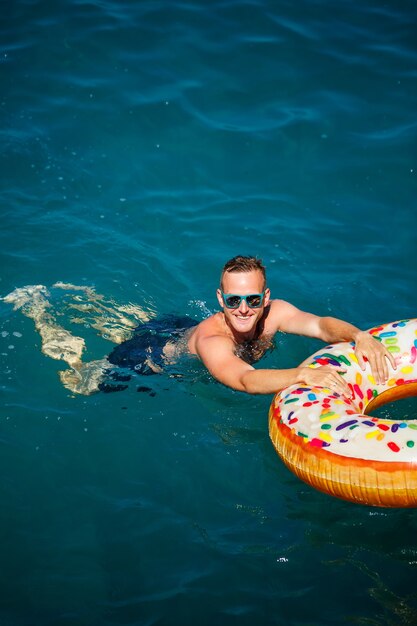 Junger Mann auf einem aufblasbaren Ring im Meer ruht und schwimmt an einem sonnigen Tag