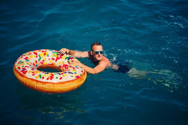 Junger Mann auf einem aufblasbaren Ring im Meer ruht und schwimmt an einem sonnigen Tag