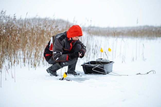 Junger Mann auf einem verschneiten See Winterfischer setzt Köder