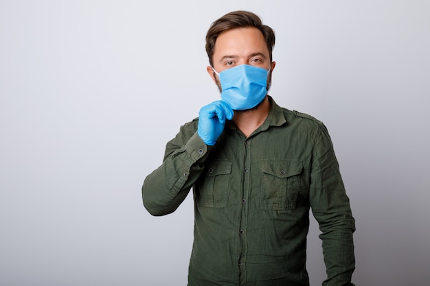 Junger Mann auf einer weißen Wand in einer medizinischen Maske auf seinem Gesicht, die gegen Coronavirus und andere Krankheiten schützt.