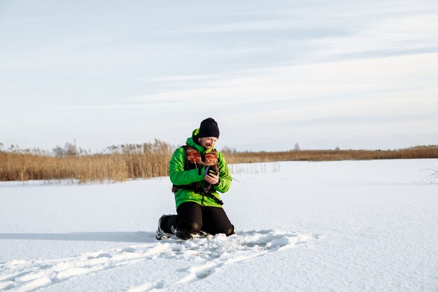 Junger Mann auf einer Winterfischerei auf einem verschneiten See fischt auf einer Angelrute