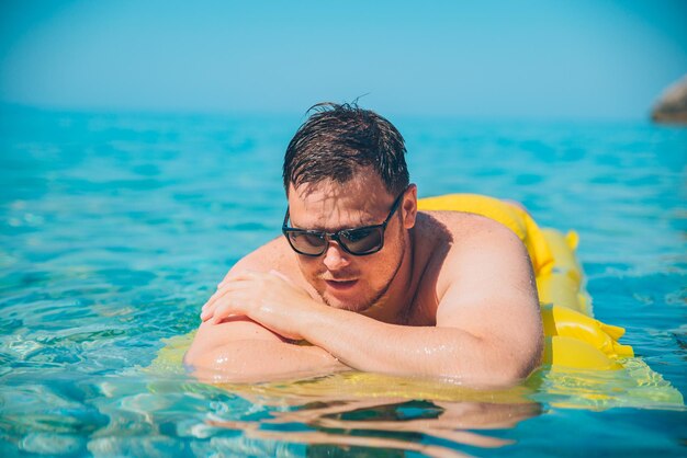 Junger Mann auf gelber Luftmatratze in klarem, transparentem Wasser