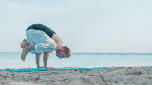 Junger Mann balanciert auf seinen Händen und praktiziert Yoga am Strand