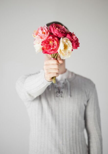 junger Mann bedeckt sein Gesicht mit Blumenstrauß.