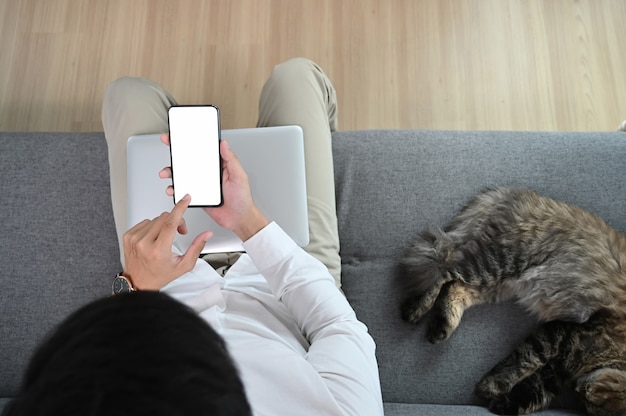 Junger Mann benutzt Smartphone und sitzt mit seiner Katze auf dem Sofa